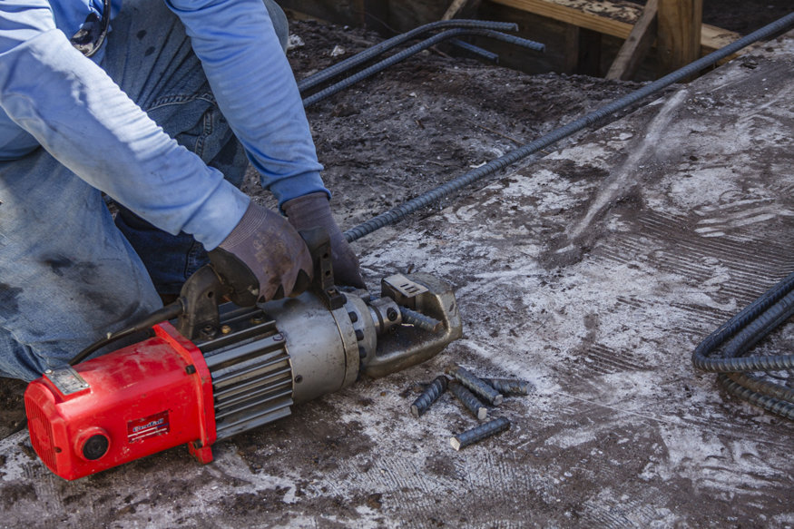 Worker cuts reinforcing steel with powered rebar tool.