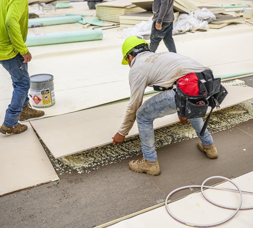 Worker positions insulation board on new roof deck.