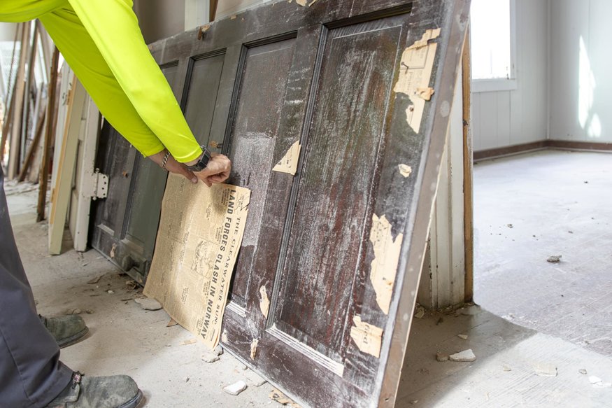 Historic newspaper sheet being pulled from door panel during interior work.
