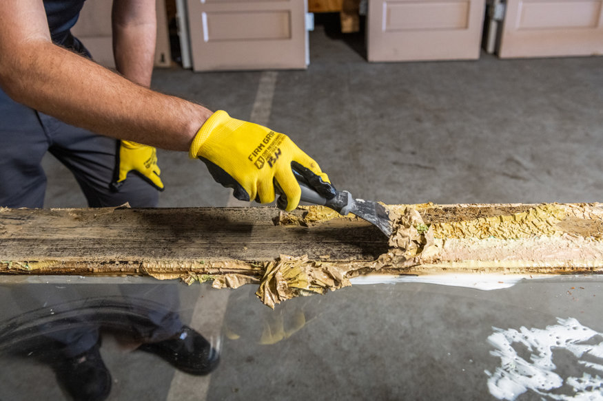 Close-up of a worker scraping paint from a historic wood door during the restoration process.