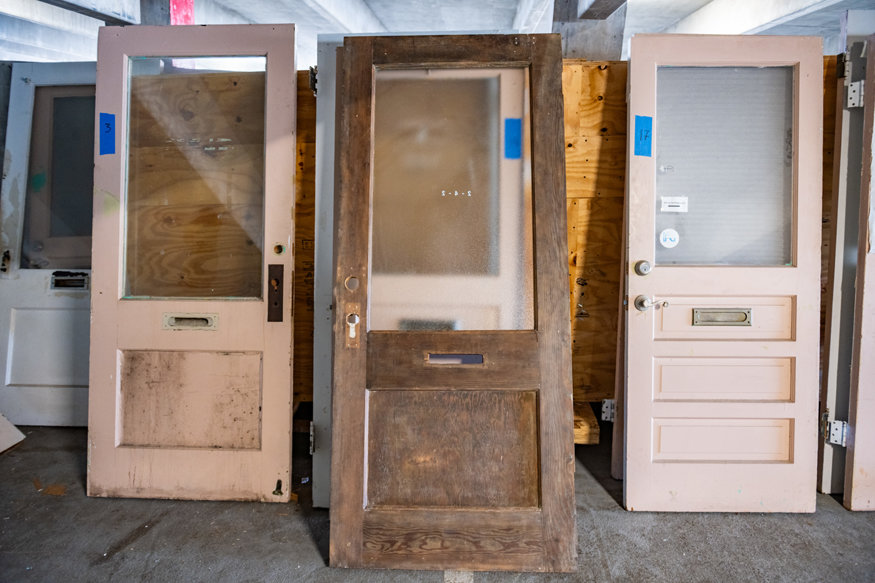 Historic interior door with exposed wood finish displayed among other doors awaiting restoration.