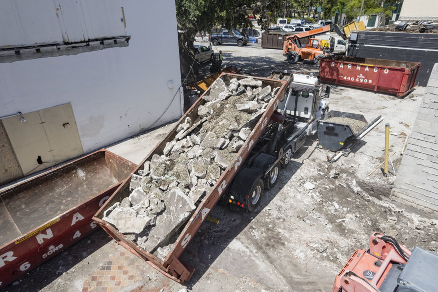 Truck loading a dumpster filled with broken concrete and demolition debris for removal.