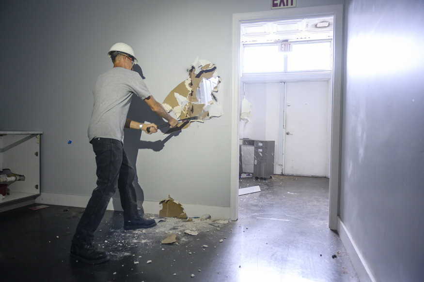 Worker using a sledgehammer to break through drywall inside the building near rear exit.