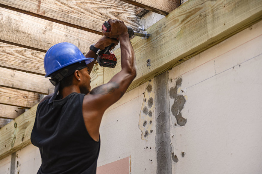 Worker fastens wood ledger to CMU wall with impact driver.
