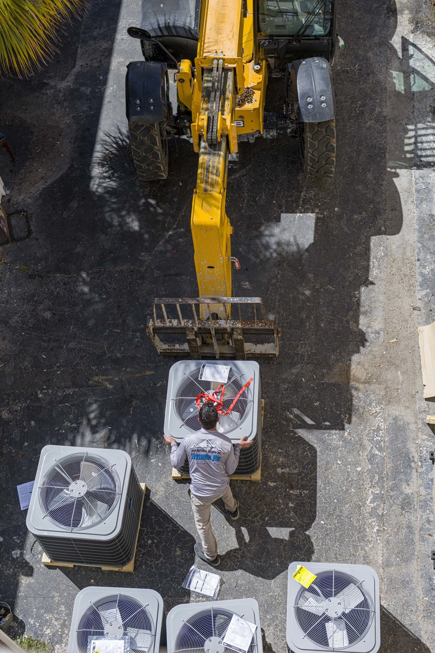 Workers preparing A/C unit for telehandler.