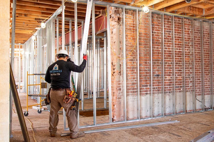 Workers securing metal stud framing on second floor.
