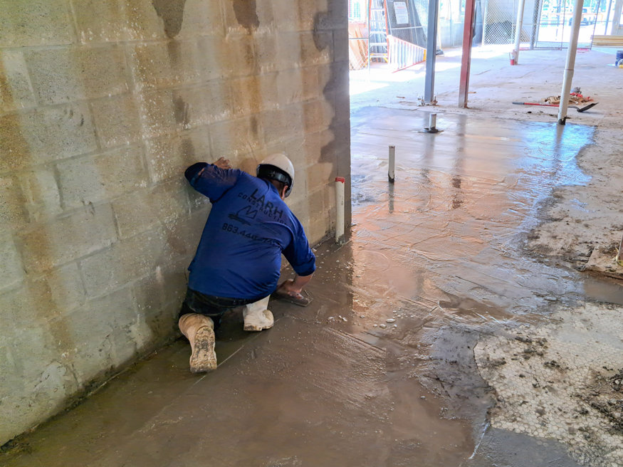 Worker smoothing concrete along wall during final trench pour at Peoples Bank.