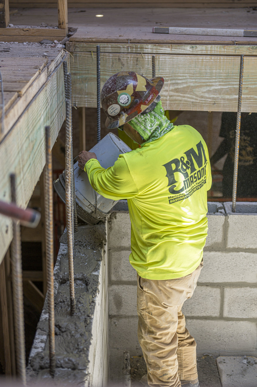 Construction worker fills hollow concrete blocks with poured concrete to reinforce the elevator shaft structure.