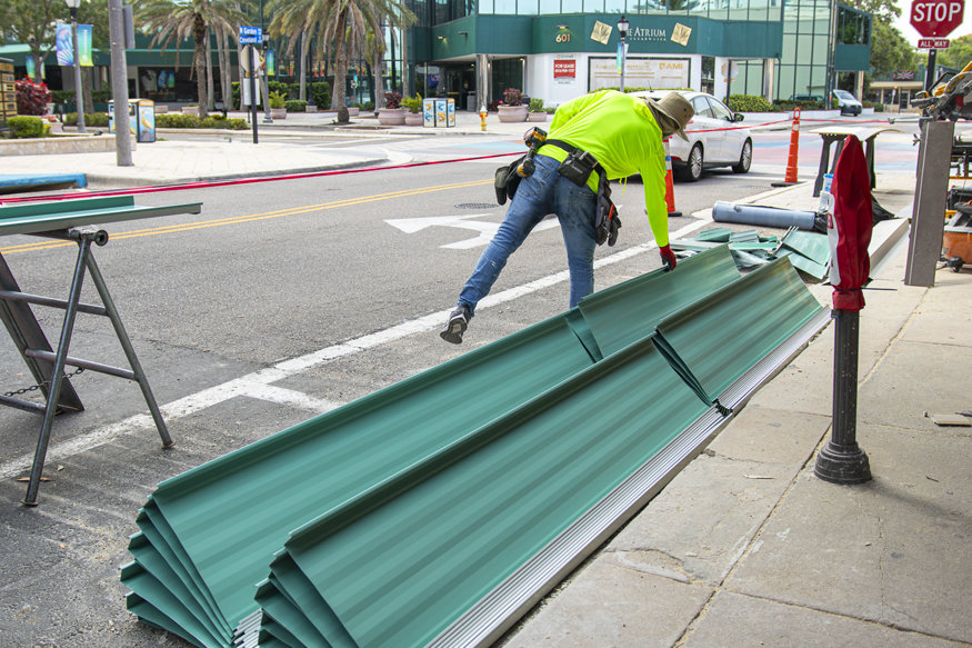 Worker examines roofing panels on sidewalk.