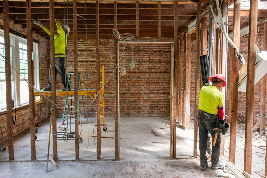 Worker cuts fasteners from historic wood studs during restoration. 