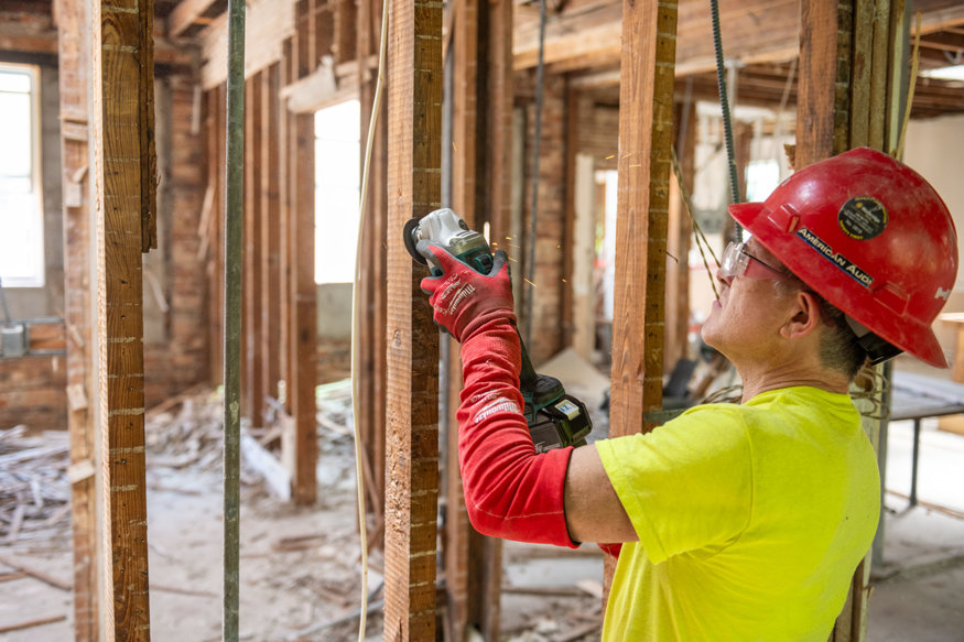 Worker cleaning base of wood studs during interior restoration