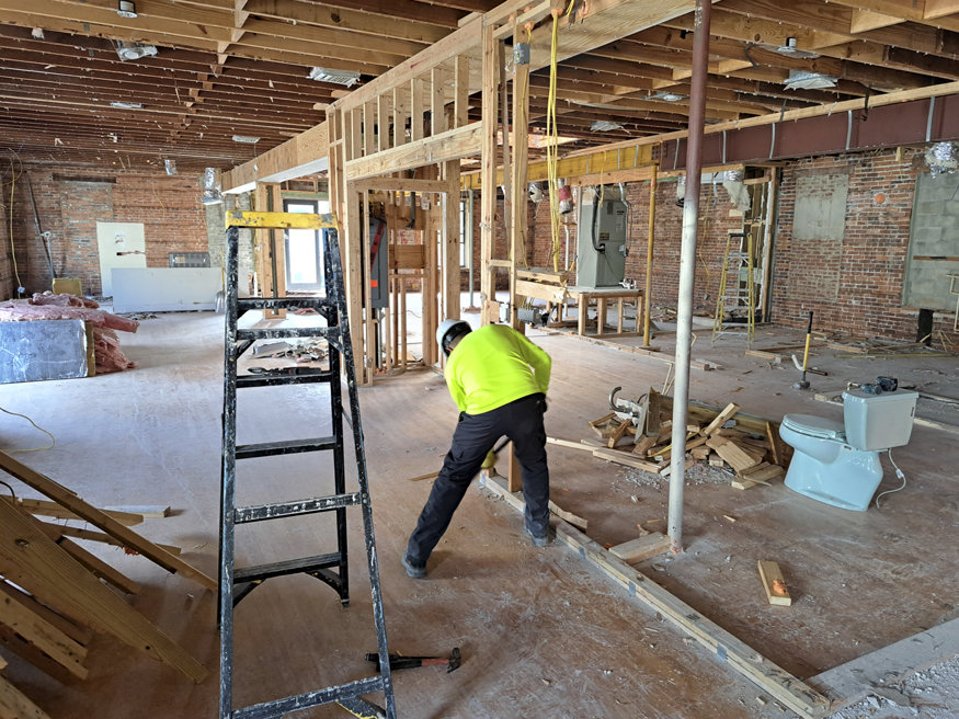  Construction worker clears debris during the interior demolition of a historic building, exposing wooden framing and original structural elements.