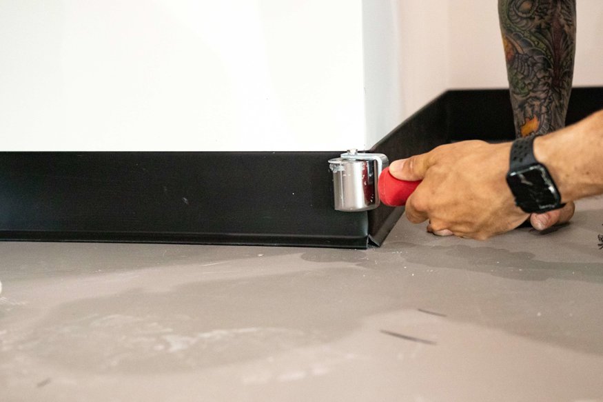 Workers installing black rubber base along interior walls. 