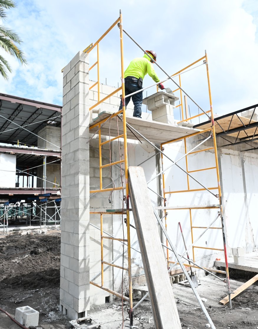 Worker applies mortar to concrete blocks during front wall reconstruction.