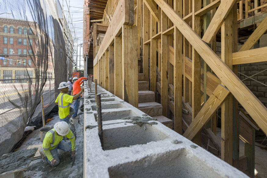 Reinforced concrete is being poured at the base of the demolished east wall foundation.