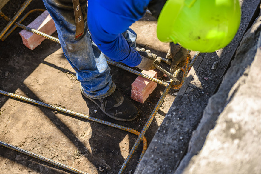 Worker ties intersecting reinforcing bars in footing.