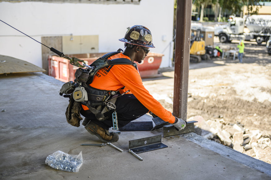 Worker aligns steel bracket at building edge.