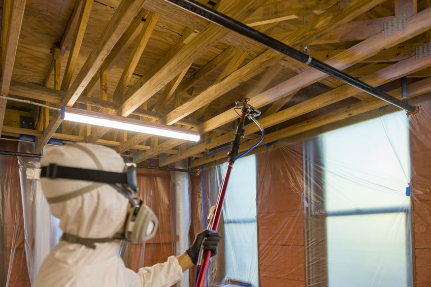  Close-up of a crew member spraying shellac on wooden ceiling beams.