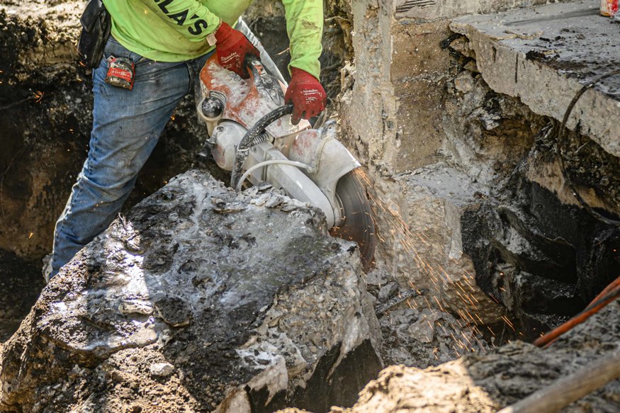 Worker uses concrete saw during footing excavation.