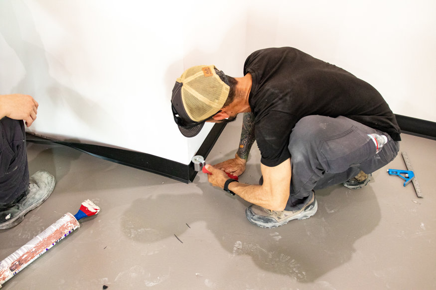 Installer rolls rubber base into interior wall corner. 