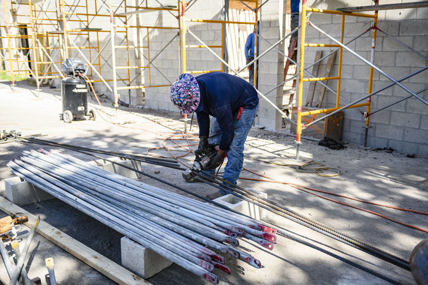 Worker cuts rebar with powered cutting tool.