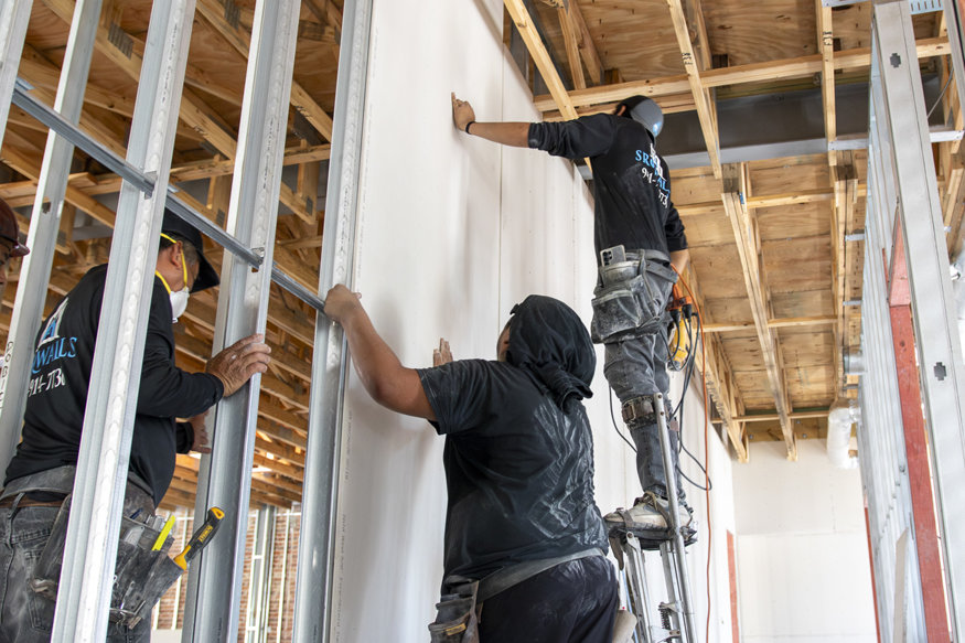 Crew aligning drywall on framed walls.