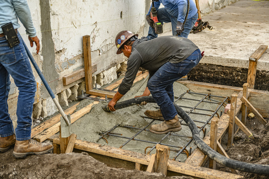 Worker places concrete into reinforced footing form.
