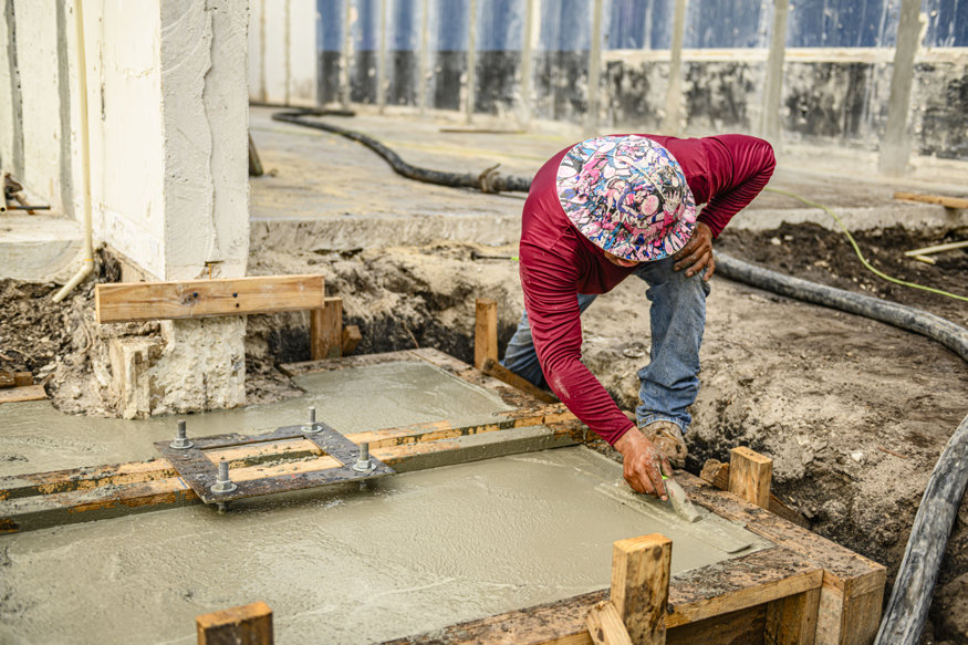 Worker finishes concrete in footing form.