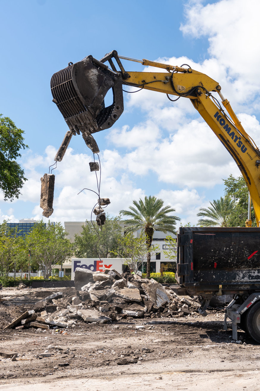 Excavator bucket holds concrete and rebar above demolition debris. 