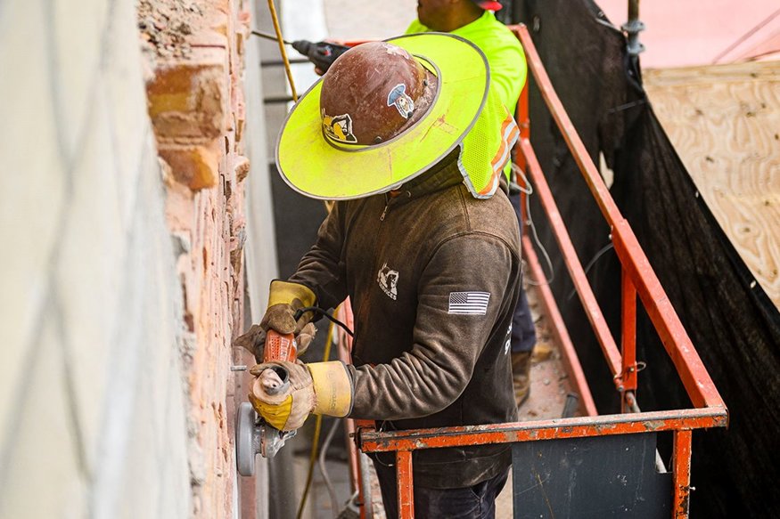 Worker removes uneven brick to prepare for mortar coating.