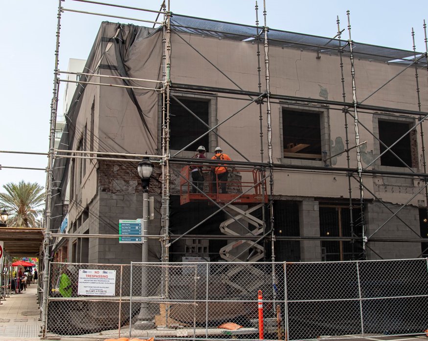 Stucco demolition begins behind protective scaffolding.