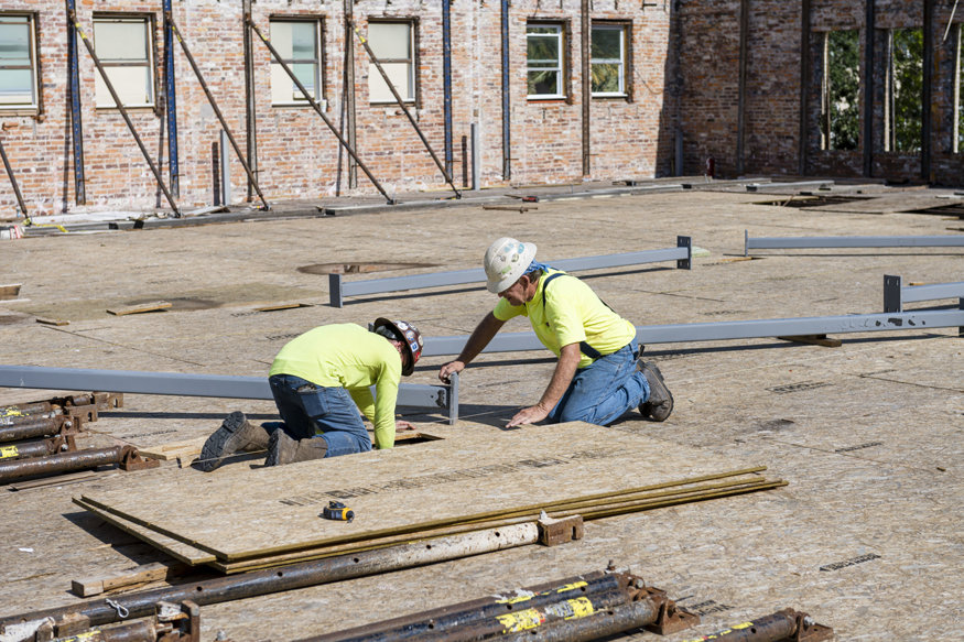 Workers align base plate for steel column on second floor.