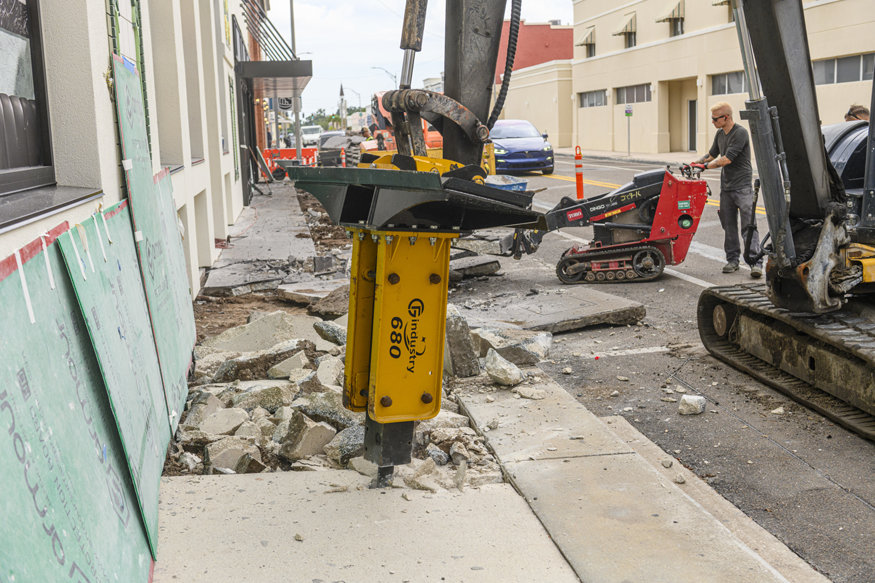 Worker using excavator to remove concrete sidewalk. 