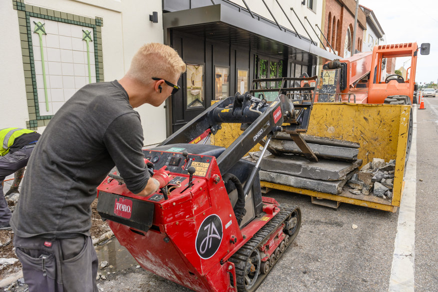 Skid steer clearing demolished sidewalk materials outside Peoples Bank building.