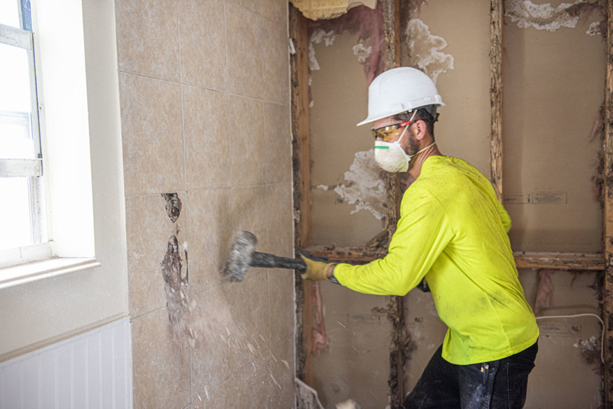 Demolition crew member exposing the wall for plumbing removal.