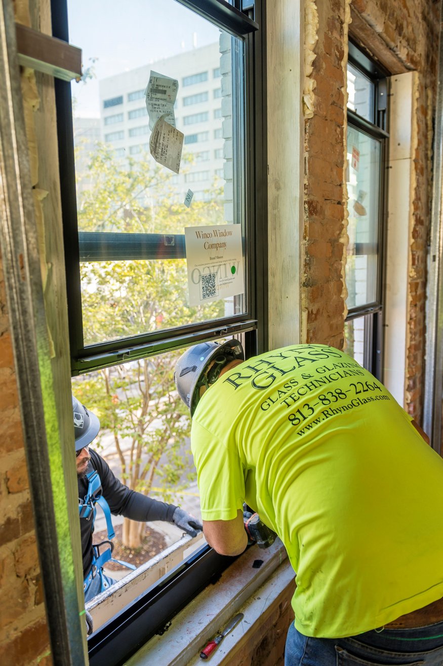 Workers fitting window frame into second-floor opening.