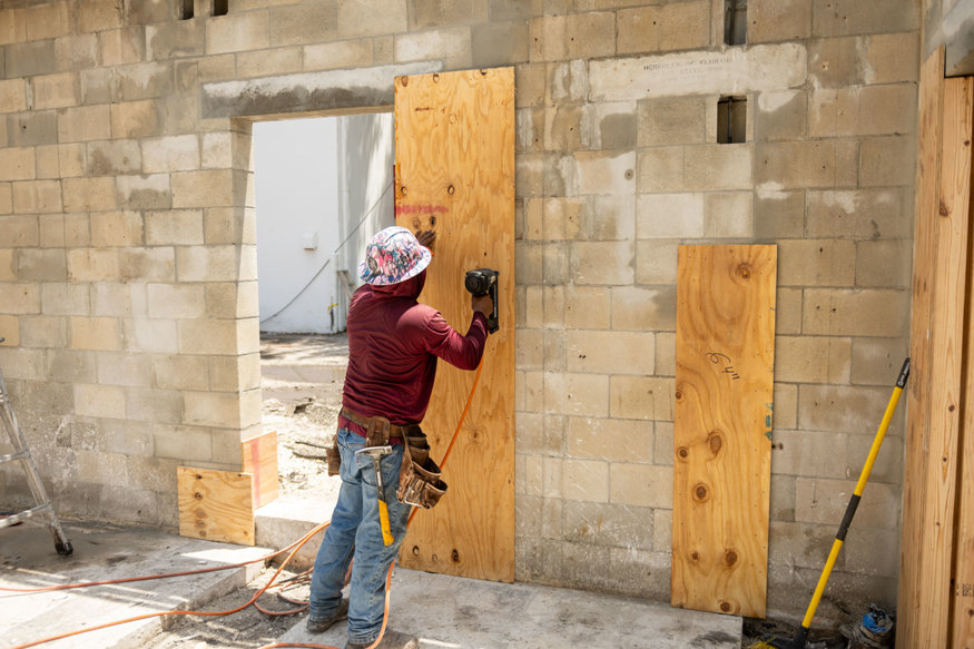 Worker secures plywood formwork over a concrete masonry wall opening.