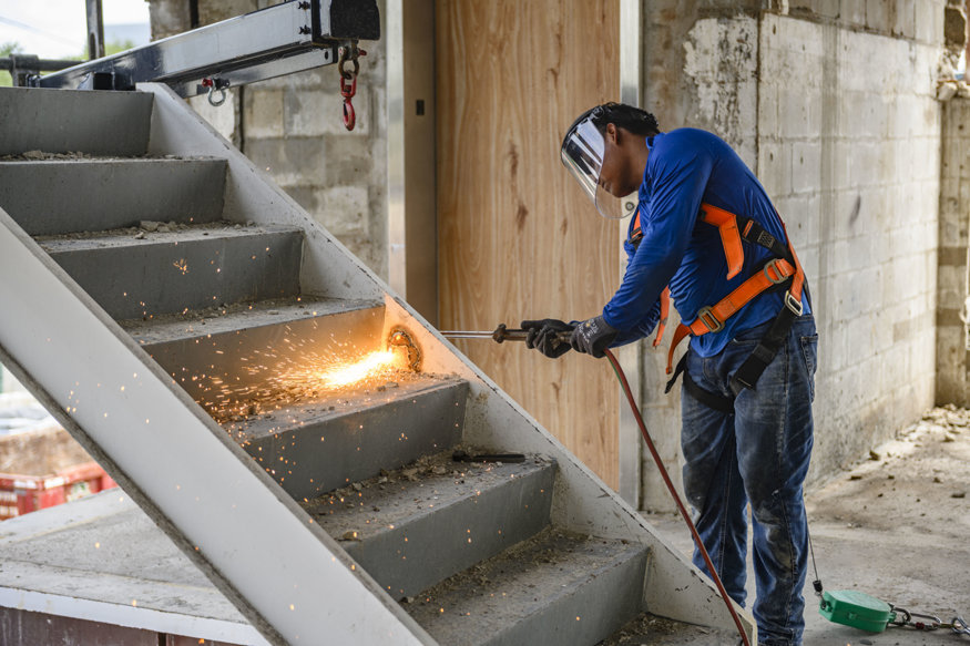 Worker cutting steel stair structure with torch inside building.