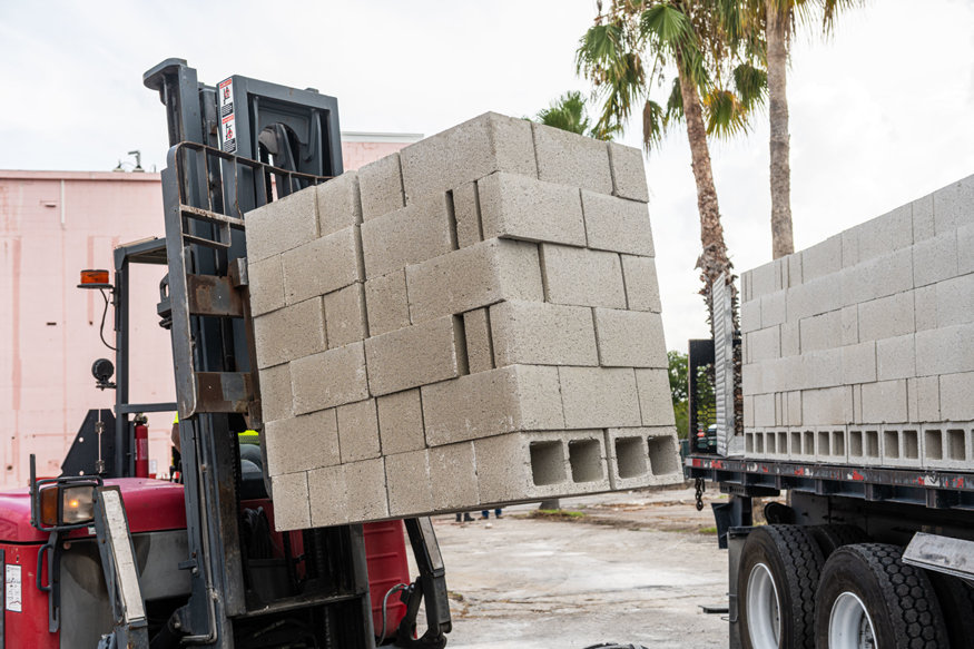 Forklift unloads concrete blocks from delivery truck.