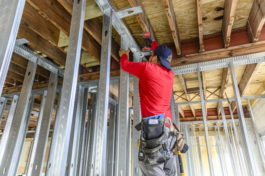 Worker fastens metal framing with cordless driver.