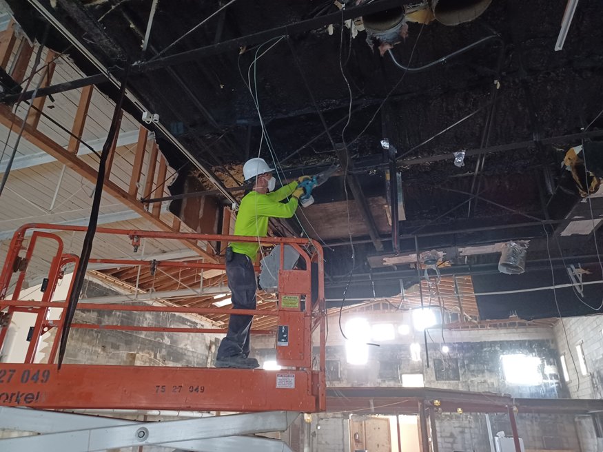 Workers removing ductwork from the ceiling interior.