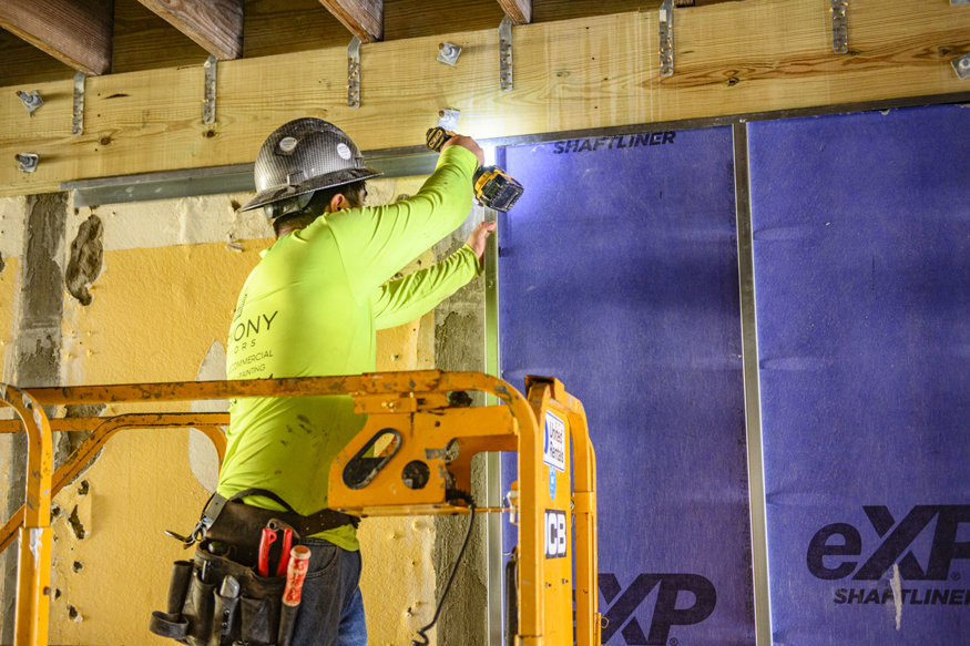 Worker fastens metal framing around a shaft-wall liner.
