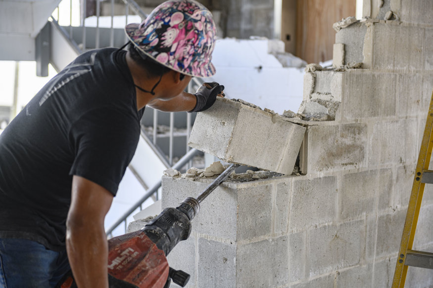 Worker removes concrete block wall during interior stairwell demolition.