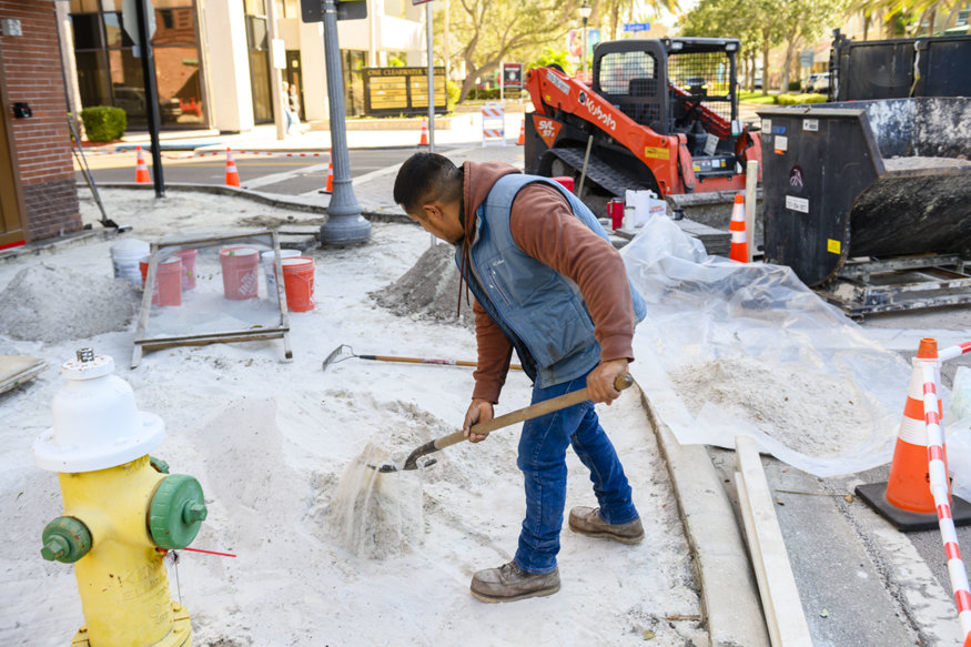 Worker shoveling base material into sidewalk area.