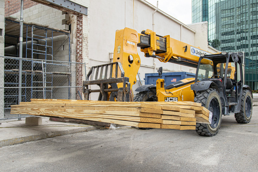 Forklift holding a bundle of new wooden truss beams at a construction site, ready for structural repairs.