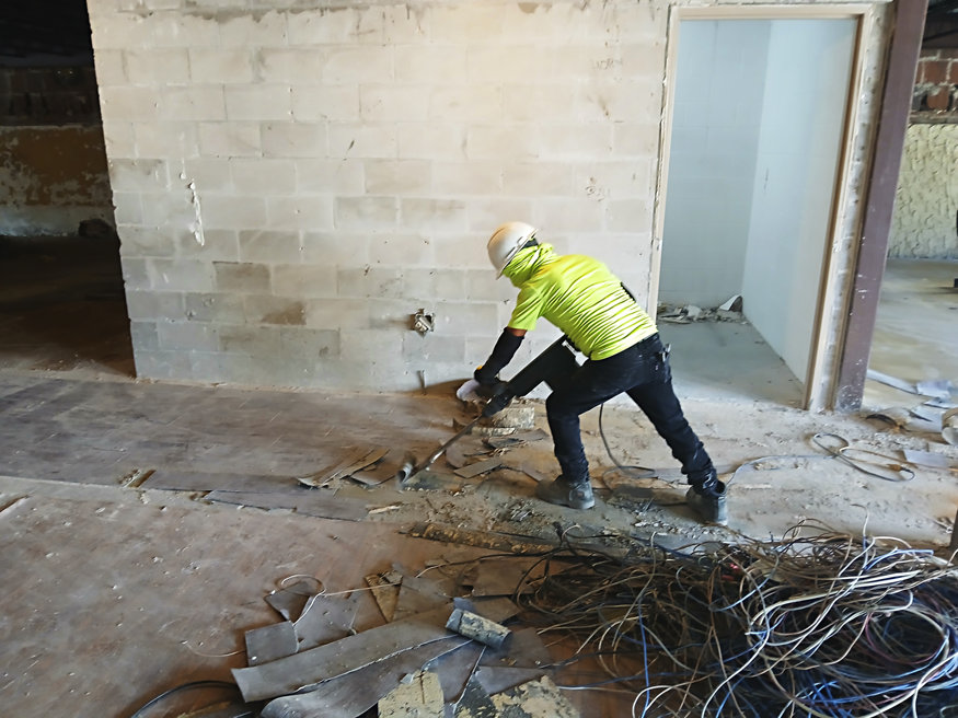 A construction worker removing flooring with tools near a block structure inside a building under renovation.