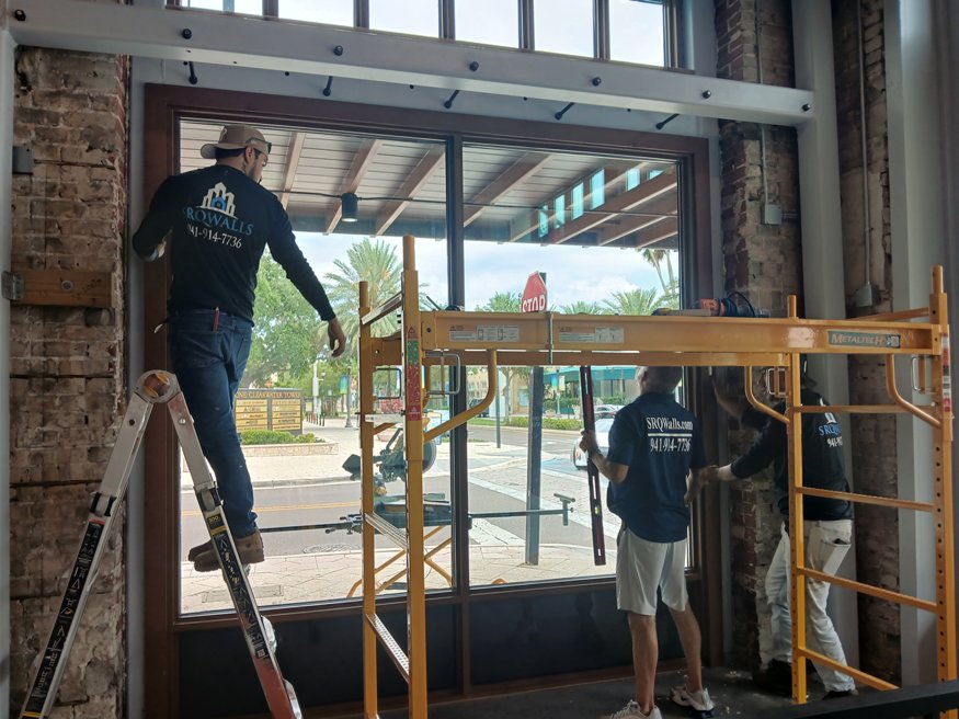 Workers using ladders and scaffolding to install interior wood trim around large storefront windows at the telephone building.