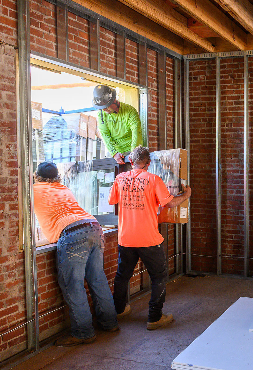 Workers moving windows through wall opening.