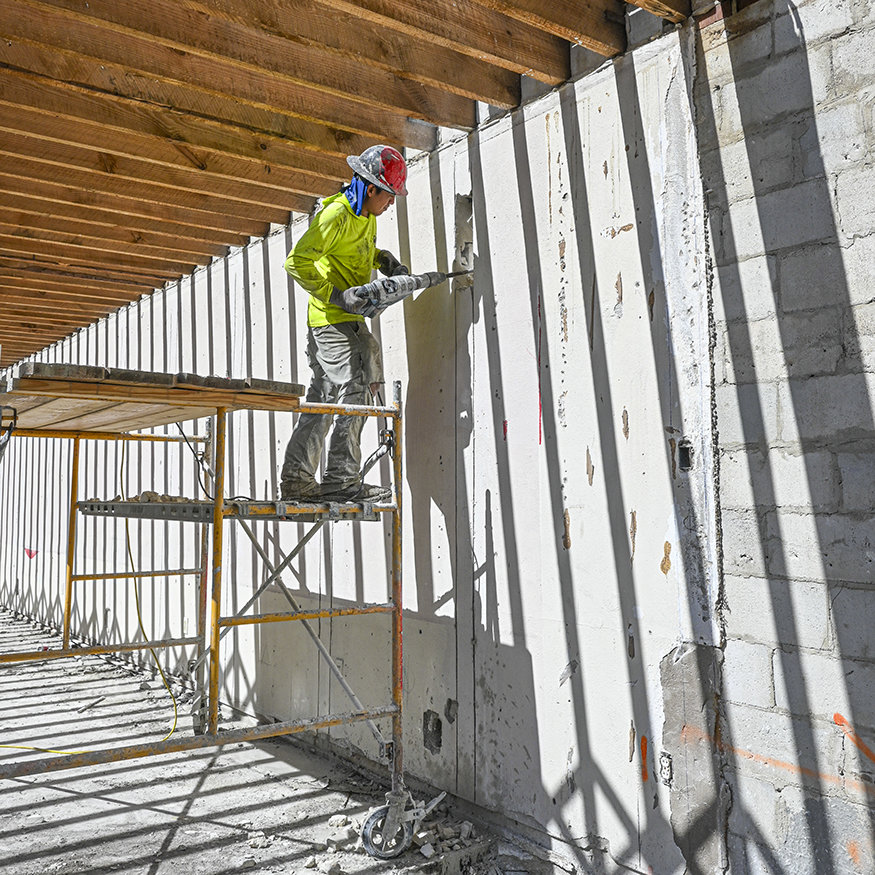 Worker uses rotary hammer to open wall channel.