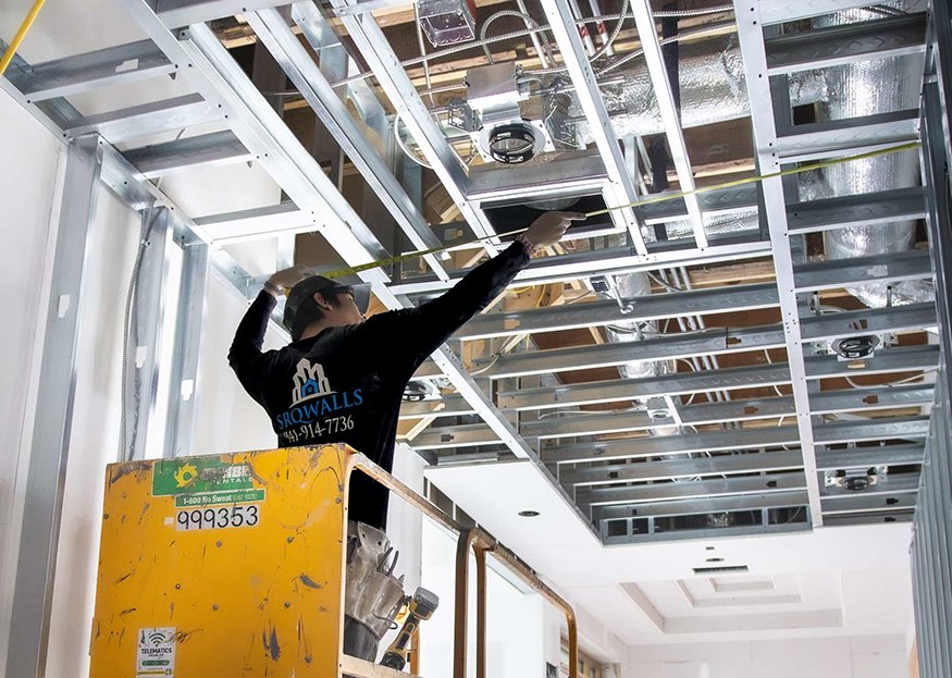 Worker measuring metal ceiling framing grid from lift.